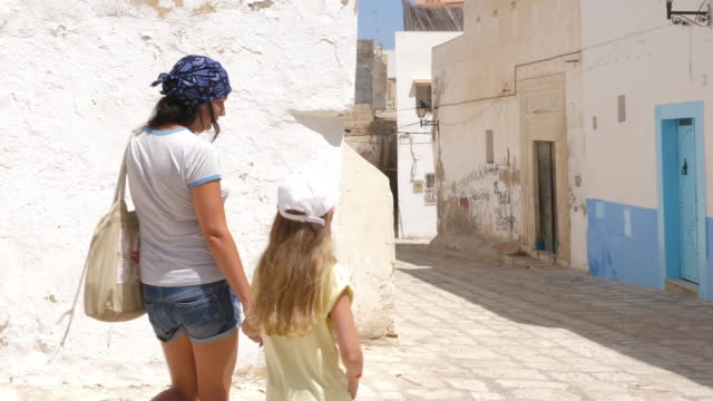 Mom-with-her-daughter-walking-by-old-town-street