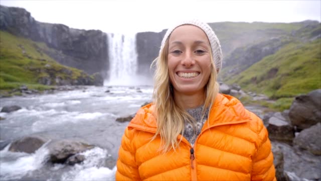 Portrait-of-blond-hair-woman-front-of-magnificent-waterfall-in-Iceland