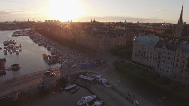 Luftaufnahme-des-Stockholmer-Stadtbild-bei-Sonnenuntergang.-Drohne-Schuss-fliegt-über-Kanal,-Straße-und-Gebäude.-Verkehr-und-Straßenbahn-Auto-vorbei,-Hauptstadt-von-Schweden