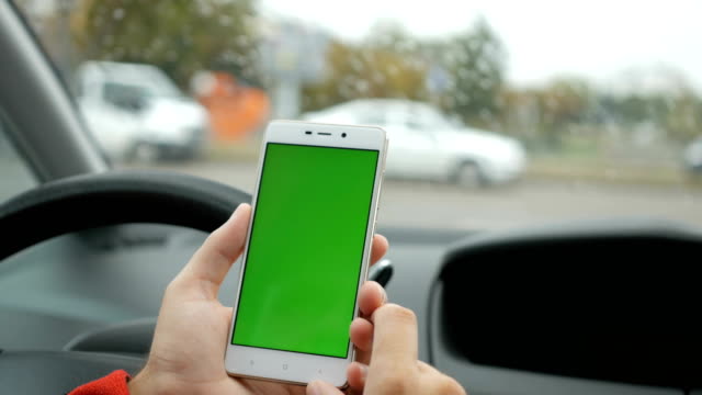 Hand-mit-Smartphone-mit-grünen-Bildschirm-im-Auto-Richtung,-Massage,-Lage,-Geschäft.-Leben-in-der-Stadt.-Mann-im-Auto-sitzt-und-arbeitet-an-Smartphone-green-Screen-Closeup.-Chroma-Key.-Regnerischen-Tag.
