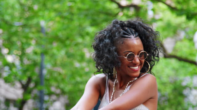 Trendy-young-black-woman-wearing-round-sunglasses-and-camisole-having-fun-and-laughing-outdoors,-close-up