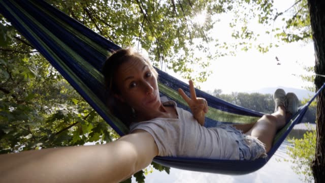 Junge-Frau-nehmen-Selfie-auf-entspannende-Hängematte-am-Fluss-im-Sommer.-SELFIE-Zeit