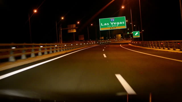 Por-la-carretera/la-autopista-en-la-noche,-señal-de-salida-de-la-ciudad-de-Las-Vegas,-Nevada