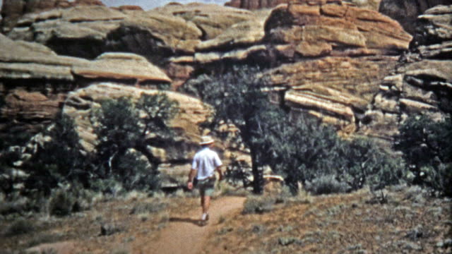 DE-CANYONLANDS,-UTAH--1971:-Hombre-caminatas-estrecho-canyon-senderos-formaciones-rocosas.