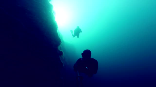 Deep-Freedivers-Erkunden-einer-Seite-von-einem-Unterwasser-Klippe