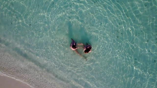 v03999-Aerial-flying-drone-view-of-Maldives-white-sandy-beach-2-people-young-couple-man-woman-romantic-love-on-sunny-tropical-paradise-island-with-aqua-blue-sky-sea-water-ocean-4k