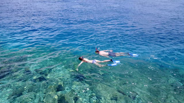 v04058-vista-aérea-de-drone-volando-de-Maldivas-playa-2-personas-pareja-joven-hombre-mujer-snorkel-natación-buceo-en-la-isla-de-paraíso-tropical-soleado-con-cielo-azul-aqua-agua-mar-4k