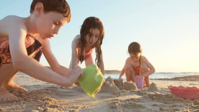 Three-kids-playing-on-the-beach-building-sand-castles-together
