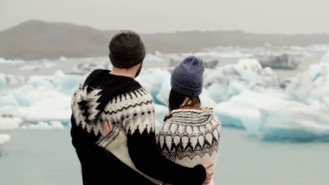 Vista-posterior-de-pie-de-joven-pareja-en-la-laguna-de-hielo.-Hombre-besa-a-la-mujer-y-la-abraza,-en-los-glaciares-en-Islandia