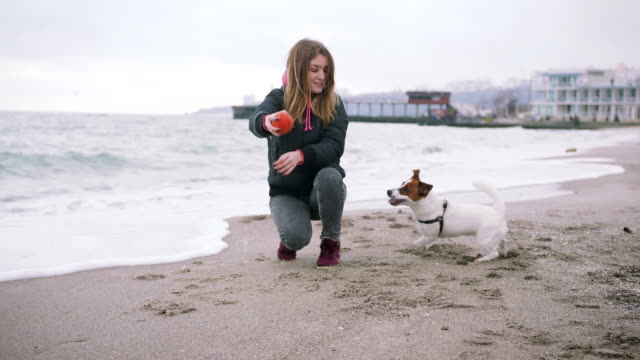 Junge-Frau-mit-Hund-Jack-Russel-am-Strand-am-Meer,-Zeitlupe-spielen
