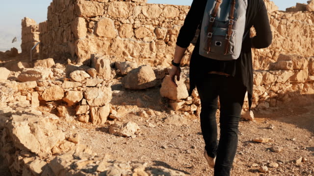 Hombre-con-pasos-de-mochila-en-paredes-antiguas-ruinas.-Turismo-hombre-caucásico-caminatas-sobre-grandes-rocas-amarillas.-Masada-Israel-4K