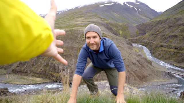 Excursionista-ayuda-a-su-compañero-de-equipo-para-llegar-a-la-cima-de-la-montaña-sobre-el-cañón-en-Islandia
