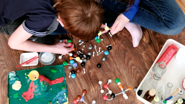 Closeup-hands-of-mom-and-son-building-molecule-models-of-colored-plastic-construction-set.-Top-view.