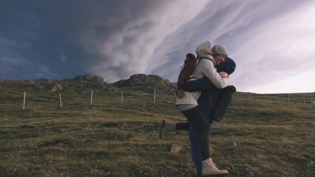 Young-loving-couple-hugging-in-field-on-background-of-epic-dramatic-clouds,-slow-motion