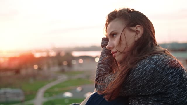 Portrait-of-beautiful-sad-European-young-woman-on-roof-or-balcony-or-terrace-enjoying-sunset