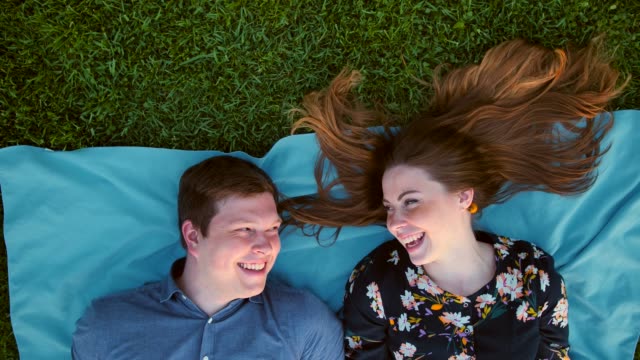 Happy-young-adult-couple-lying-on-the-grass-over-sunset