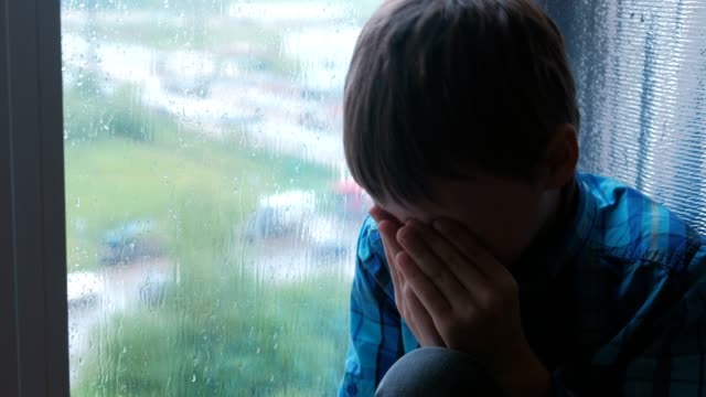 Crying-boy-looks-out-the-window-in-the-rain-and-is-sad.