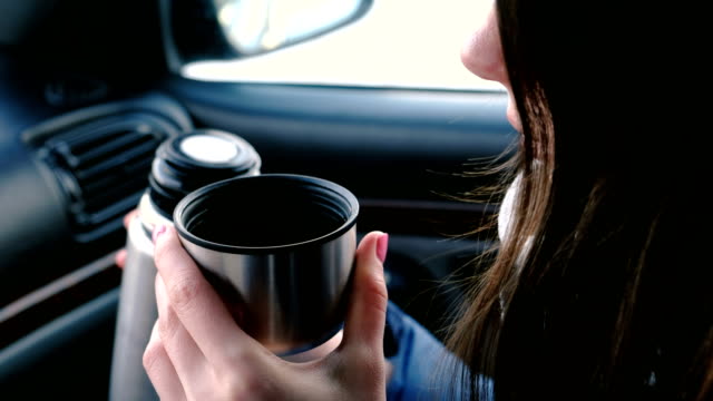 Detailansicht-unkenntlich-Frau-aus-Thermoskanne-sitzen-im-Auto-im-Winter-einen-heißen-Tee-in-eine-Tasse-trinken.