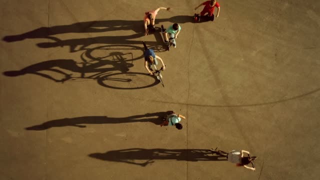 Children-cycling,-roller-skating-and-scootering-cast-long-shadows.-Top-view,-slow-motion