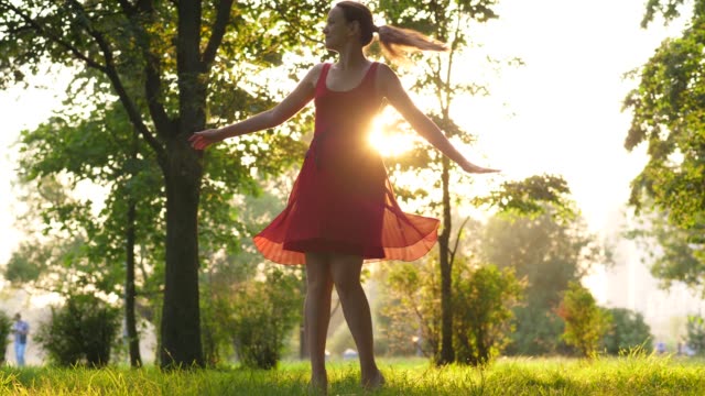 Mujer-riendo-feliz-en-vestido-rojo-bailando-y-girando-alrededor,-brilla-el-sol-a-través-de-la-falda-transparente