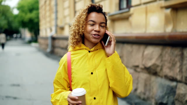 Schönes-Afroamerikanisches-Mädchen-ist-telefonieren-mit-Handy-und-halten-nehmen-Weg-Kaffee-im-Stadt-Straße-entlang-spazieren-und-genießen-Gespräch-lachen.