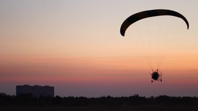 The-pilot-on-a-paraglider-flies-from-the-camera-gradually-moving-away-into-the-distance-against-the-sunset-beautiful-sky