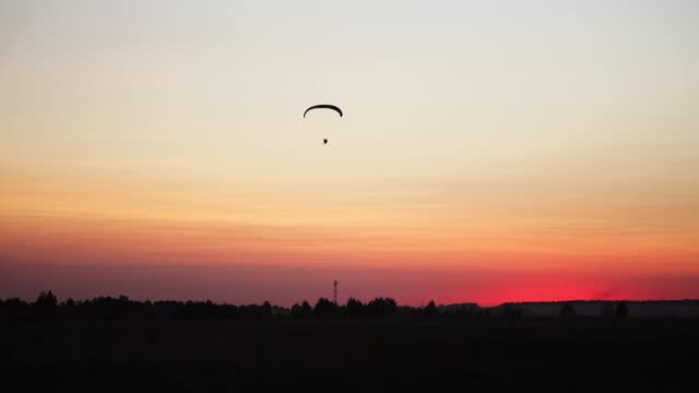 Der-Pilot-auf-einem-Gleitschirm-fliegt-von-der-Kamera-allmählich-Weg-in-die-Ferne-gegen-den-Sonnenuntergang-schönen-Himmel.-Schöner-Hintergrund-Hintergrundbild.-Begriff-der-Freiheit
