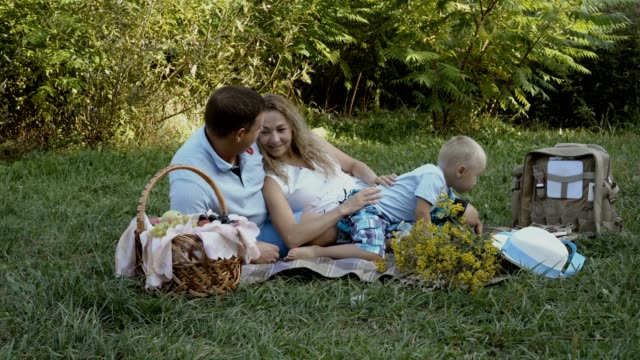 Glückliche-Familie-hatten-ein-Picknick-in-der-Natur.-Mama,-Papa-und-Sohn-liegen-und-spielen-auf-dem-Rasen-im-Park.