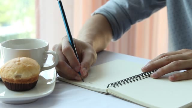 Empresario-o-estudiante-holding-pluma-escribir-libro-y-tomando-café-en-la-mesa-de-la-mañana.