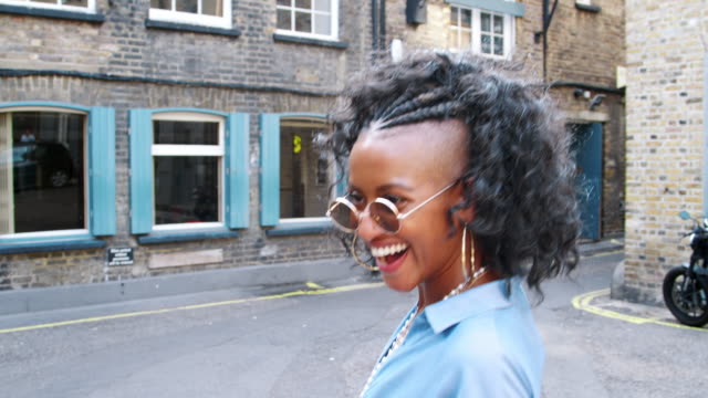 Trendige-junge-schwarze-Frau-in-blauem-Kleid-und-eine-Sonnenbrille,-die-auf-der-Straße-lachen,-Rückansicht,-Nahaufnahme