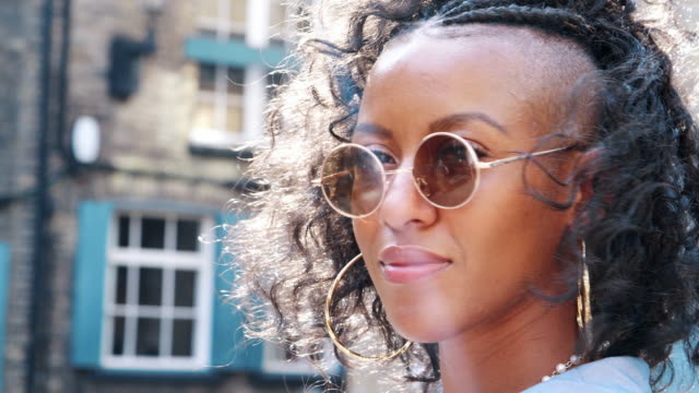 Trendy-young-black-woman-wearing-round-sunglasses-turns-to-look-to-camera,-head-shot,-side-view