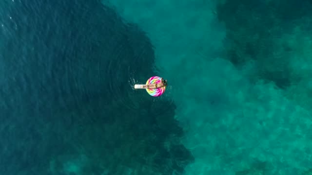 Aerial-view-of-woman-floating-on-inflatable-lollipop-on-Atokos-island,-Greece.