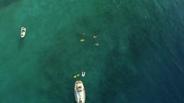 Aerial-view-of-group-swimming-with-inflatable-mattress-next-to-boat,-Greece.