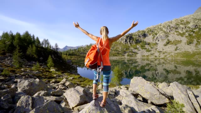 Young-woman-standing-by-stunning-alpine-lake-in-the-Swiss-Alps-arms-wide-open-to-embrace-nature.-woman-arms-outstretched-success-and-freedom-concept