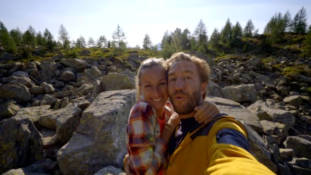 Wanderer,-paar-unter-Selfie-Porträt-auf-Bergweg.-Sonne-über-den-Bergen.-Schöne-Sonnenstrahl-Effekt-macht-eine-idyllische-Landschaft.-Junges-Paar-Wandern-nehmen-video-Selfie-in-der-Schweiz