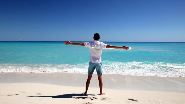 Young-man-standing-on--beach-with-outstretched-hands
