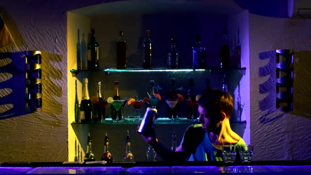 Barman-joven-haciendo-trucos-con-dos-copas,-un-agitador-y-botella-standing-behind-the-bar,-ver,-tirando-en-cámara-lenta