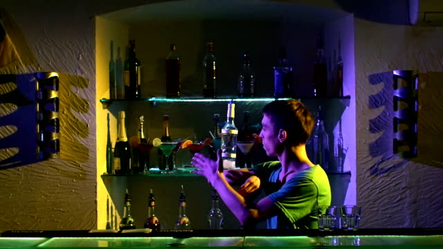 Barman-joven-haciendo-trucos-con-dos-copas-y-una-botella-standing-behind-the-bar,-ver,-tirando,-cócteles,-cámara-lenta
