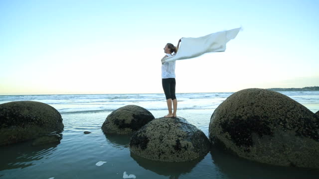 One-female-stands-on-boulder,-holds-blanket-in-the-air