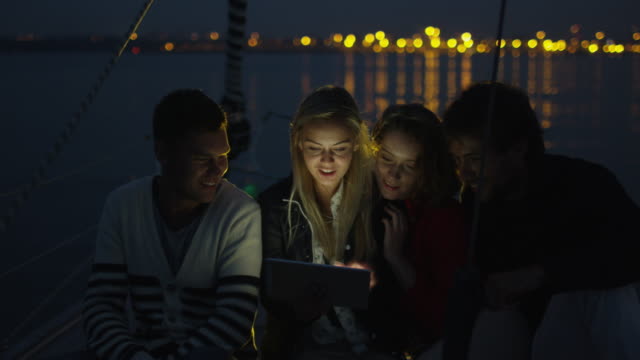 Gruppe-von-Personen-mit-Tablet-auf-einem-Segelboot-im-Meer-in-der-Nacht.