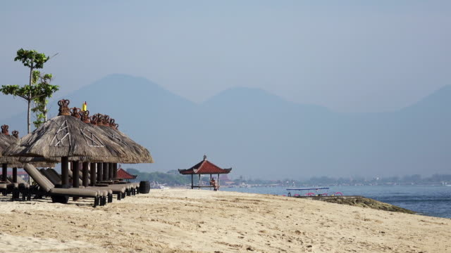 Wellen-des-warmen-Meeres-laufen-am-Sandstrand-des-tropischen-Resorts-mit-Sonnenschirmen-und-Liegestühlen
