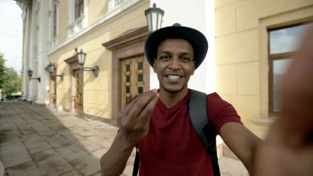 Happy-mixed-race-tourist-man-having-online-video-chat-using-his-smartphone-camera-standing-near-historical-building-in-Europe