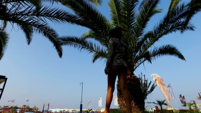 Rear-view-of-Attractive-girl-walking-on-beach-under-palm-trees,-low-angle