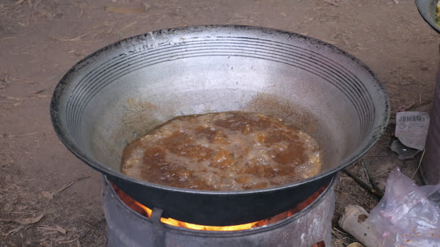 Mann-stürzt-Fisch-in-heißem-Öl-Wok-Kochen-über-behelfsmäßigen-Feuerstelle-(Nahaufnahme)
