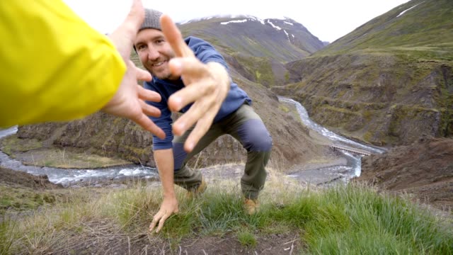 Excursionista-ayuda-a-su-compañero-de-equipo-para-llegar-a-la-cima-de-la-montaña-sobre-el-cañón-en-Islandia