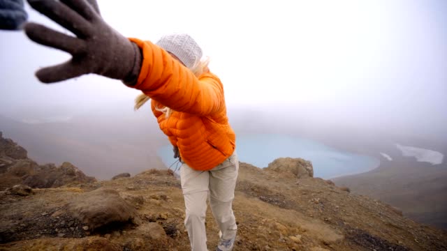 Young-woman-hiking,-pulls-out-hand-to-reach-the-one-of-teammate.-A-helping-hand-to-reach-the-mountain-top.-Hiker-assists-teammate-to-reach-mountain-top-above-volcanic-crater-lake-in-Iceland