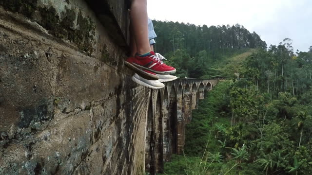 4K-UHDTV:-Mother-and-son-siting-and-swing-one's-feet-on-the-Demodara-nine-arches-bridge-in-Ella,-Sri-Lanka:-close-up-feet-image