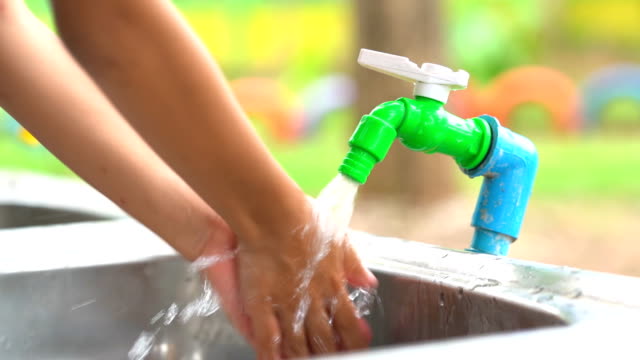 Water-tap-open-pouring-water-to-cleaning-hand-of-child.-Clean-water-flowing-out-from-vale-pipe-to-sink.-Close-up-hand-and-faucet-water-tap
