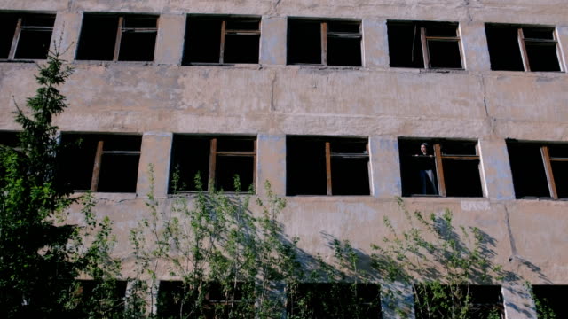 Woman-standing-on-window-of-destroyed-multi-storey-building-with-many-broken-windows.