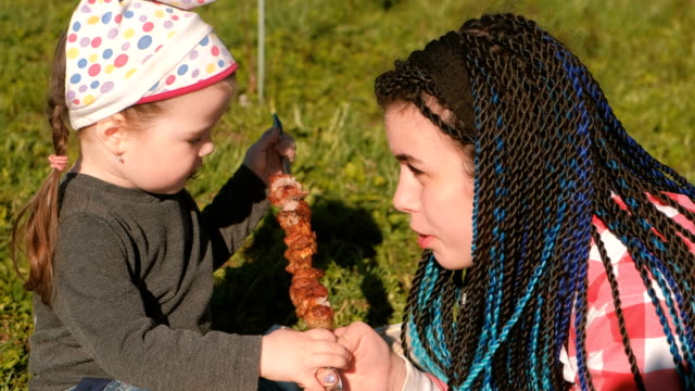 Mom-feed-her-cute-little-daughter-with-meat-shashlik-barbecue-on-a-skewer-in-the-backyard.